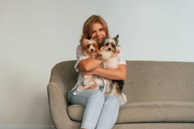 Hayvanları kucaklamak ve kucaklamak. Kadın kanepede iki sevimli köpekle oturuyor..