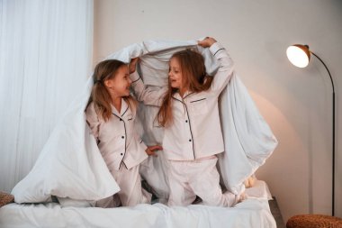 Yatak odasında, ellerinde battaniyeyle. İki küçük kız evcil odada oynuyorlar ve eğleniyorlar..