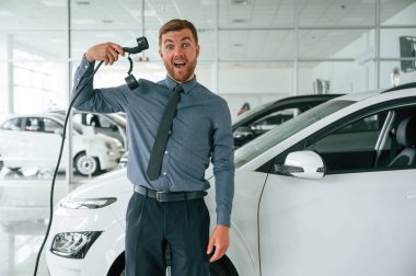 Şarj aleti ile eğleniyorum. Yakışıklı araba galerisi çalışanı elektrikli araçla çalışıyor..