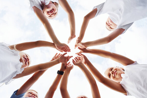 Вид снизу на детей, которые держатся за руки. На белом небе.