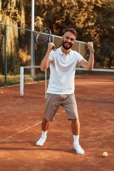 Zaferi kutluyoruz. Genç adam güneşli bir günde tenis kortunda..
