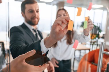 Proje planları. Ofisteki bir grup iş arkadaşı camın üzerine çıkartma yapıştırıyor..