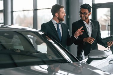 Gri renkli otomobilin yanında. İki işadamı araba galerisinde birlikte çalışıyorlar..