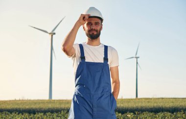 Yakışıklı servis mühendisi sahada yel değirmenleriyle duruyor..
