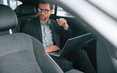 Dizüstü bilgisayarla, çalışıyor. Resmi iş elbiseli adam modern otomobilde oturuyor..