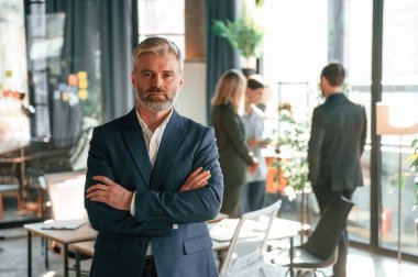 Resmi giysili yakışıklı adam ayakta duruyor. Bir grup iş adamı modern ofiste çalışıyor..