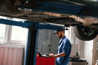 Laptop ve test cihazı kullanılıyor. Otomobil tamircisi garajda çalışıyor. Onarım servisi.
