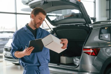 Kutu ve not defteriyle. Mavi üniformalı adam araba servisinde çalışıyor..