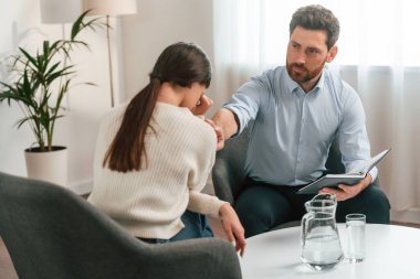 Kadın terapi seansında ağlıyor. Resmi kıyafetli doktor dolapta çalışıyor..