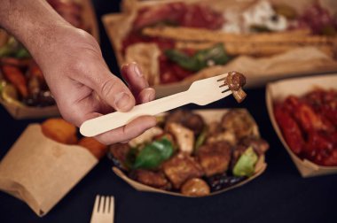 Adam mantarlı çatal tutuyor. Masanın üzerinde yemek olan manzarasını kapat. Et, sebze..