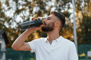 Su içmek, ara vermek. Genç adam güneşli bir günde tenis kortunda..