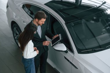 Konuşurken, tableti tutarken. Adam araba galerisindeki kadın müşteriye yeni otomobili gösteriyor..