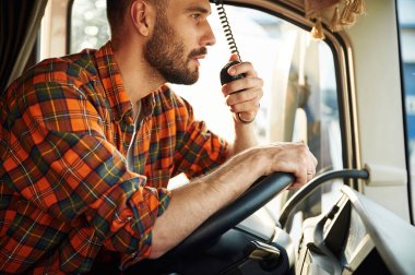 Yan görüş, aracın içinde oturuyor. Gündelik giysiler içindeki genç kamyon şoförü..