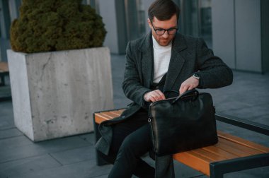 Gündüz vakti. Bankta. Resmi kıyafetli yakışıklı dışarıda, iş binasının yanında..