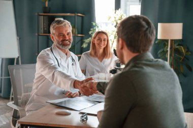 Selamlar, tokalaşıyoruz. İki doktor klinikte bir hastaya danışıyor..