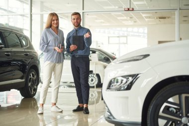 Müşteriye yardım ediyorum. Resmi elbiseli adam elektrikli arabalı bir kadınla birlikte..