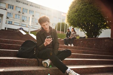 Adam merdivenlerde oturuyor. Gündelik giysiler içindeki genç öğrenciler açık havada birlikteler..