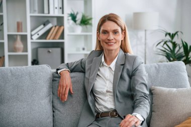 Ön manzara. Resmi elbiseli kadın evde, kanepede oturuyor..