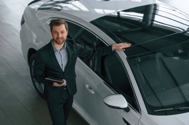 Tabletle en iyi görüntü. Siyah takım elbiseli adam otomobilin yanındaki araba galerisinde..