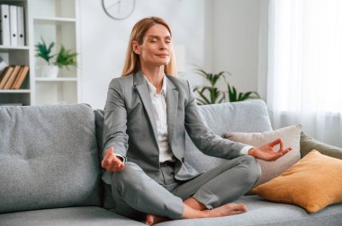 Lotus pozu, meditasyon. Resmi elbiseli kadın evde, kanepede oturuyor..