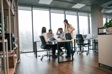 Masanın yanındaki büyük pencerelere yaslan. Ofiste birlikte çalışan dört kişi var..