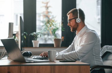 Çağrı merkezinde. Kulaklık takıyordu. Resmi kıyafetli bir ofis çalışanı bilgisayar başında oturuyor ve çalışıyor..