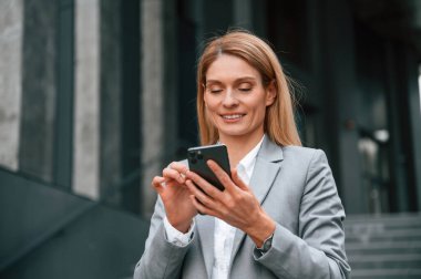 Boş zaman, yürümek, akıllı telefon tutmak. Resmi giysili kadın iş binasının yakınında dışarıda..