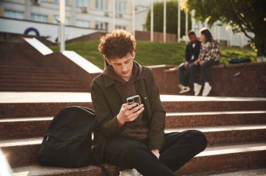 Adam merdivenlerde oturuyor. Gündelik giysiler içindeki genç öğrenciler açık havada birlikteler..