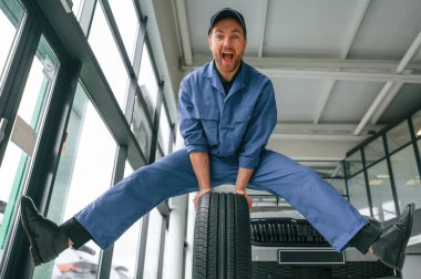 Eğleniyor, gülümsüyor, lastiklerle. Mavi üniformalı adam araba servisinde çalışıyor..