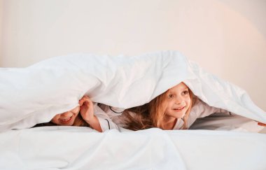 Çocuklar yatağa uzanıyorlar. İki küçük kız evcil odada oynuyorlar ve eğleniyorlar..