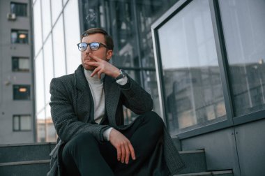 Merdivenlerde oturup sigara içmek. Resmi kıyafetli yakışıklı dışarıda, iş binasının yanında..