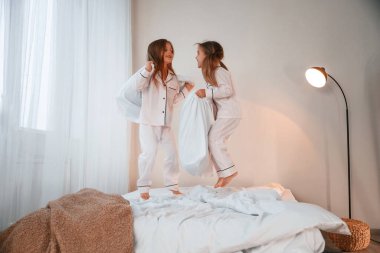 Yastıkları elinde tutarak. İki küçük kız evcil odada oynuyorlar ve eğleniyorlar..