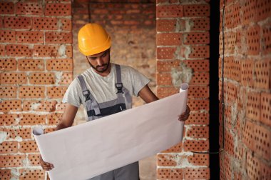 Üzerinde binanın planı olan büyük bir kağıt. Yakışıklı Hintli adam şantiyede..