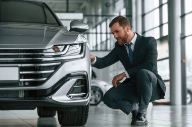 Takım elbiseli ve kravatlı adam araba galerisindeki aracın kalitesini kontrol ediyor..
