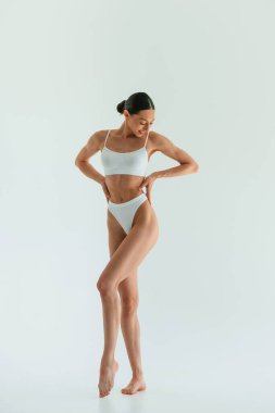 Beyaz arka plana karşı. Zayıf vücutlu genç bir kadın stüdyoda spor kıyafetleri giyiyor..