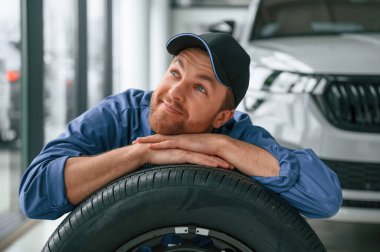Yeni lastik. Üzerine yaslan. Mavi üniformalı adam araba servisinde çalışıyor..
