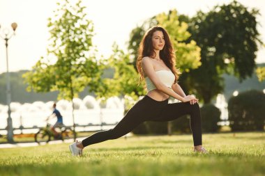 Bacak esnetme egzersizi. Spor elbiseli güzel bir kadın güneşli bir günde parkta..