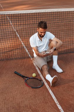 Mola verdim. Ağın yanında oturuyor. Genç adam güneşli bir günde tenis kortunda..