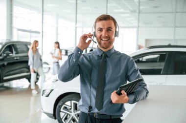 Müdür kulaklıkla ve not defteriyle birlikte. Yakışıklı araba galerisi çalışanı elektrikli araçla çalışıyor..