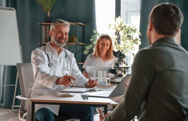 Oturup konuşmak. İki doktor klinikte bir hastaya danışıyor..