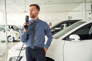 Şarj aleti ile eğleniyorum. Yakışıklı araba galerisi çalışanı elektrikli araçla çalışıyor..