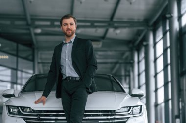 Siyah takım elbiseli adam otomobilin yanındaki araba galerisinde..