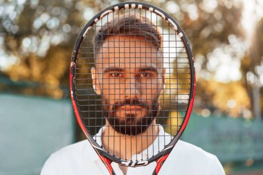 Elinde raketle dikiliyorsun. Genç adam güneşli bir günde tenis kortunda..