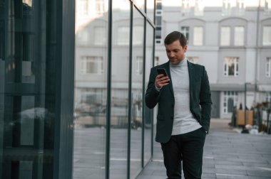 Akıllı telefonla sosyal medyayı kullanmak. Resmi kıyafetli yakışıklı dışarıda, iş binasının yanında..