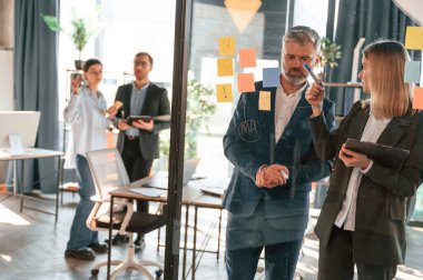 Plan kavramı. Camın üzerinde birçok çıkartma var. Bir grup iş adamı modern ofiste çalışıyor..