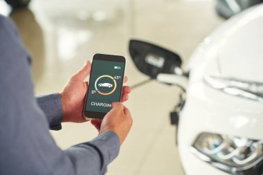 Akıllı telefon uygulaması şarj ediliyor. Elektrikli arabalı adamın yakın görüntüsü..