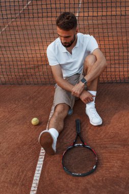 Mola verdim. Ağın yanında oturuyor. Genç adam güneşli bir günde tenis kortunda..
