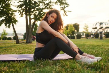 Yoga minderinde güneş ışığına karşı oturmak. Spor elbiseli güzel bir kadın güneşli bir günde parkta..