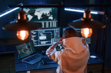 Arkadan bak. Genç profesyonel bilgisayar korsanı bilgisayar başında ve ekranlar hakkında çok fazla bilgiye sahip..