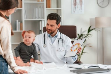 Sağlıklı yemekten bahsediyorum. Bebek ve anneyle. Resmi kıyafetli doktor dolapta çalışıyor..